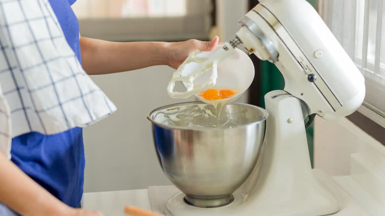 woman putting eggs into a mixer