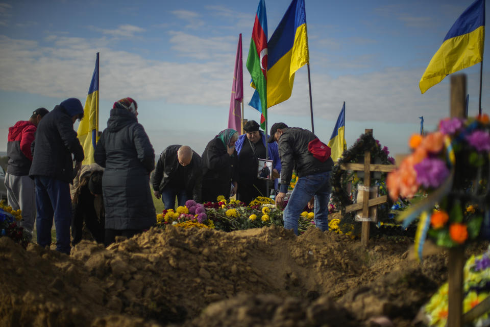 Relatives of recently killed Ukrainian serviceman Ruslan Mamedov stand next to his grave in a cemetery during Ukraine Defenders Day in Kharkiv, Ukraine, Friday, Oct. 14, 2022. (AP Photo/Francisco Seco)