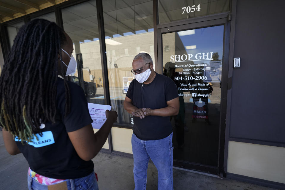 Dazmine Allen, left, of the national nonprofit Resilience Force, distributes flyers for COVID-19 testing to Kenneth McGruder, owner of Shop GHI, in New Orleans, Monday, Oct. 5, 2020. Resilience Force trains and puts to work people in the areas of disaster recovery and rebuilding with focus on Black and minority communities. (AP Photo/Gerald Herbert)