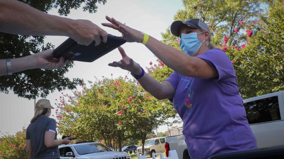 FILE - In this Tuesday Aug. 4, 2020, file photo, volunteer Wendy Dutler hands out computers during a drive-thru giveaway event in Dallas. Americans can begin applying for $50 off their internet bill on Wednesday, May 12, 2021, as part of an emergency government program to keep people connected during the pandemic. (AP Photo/LM Otero, File)