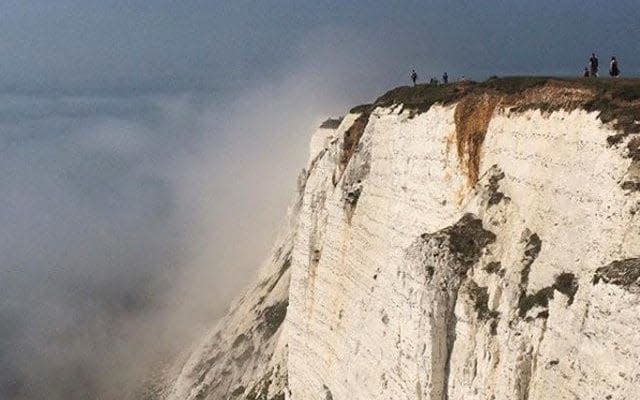 People stand on a cliff at Beachy Head amidst mist, near Eastbourne - REUTERS