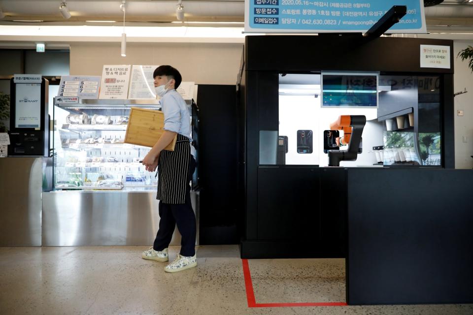 An employee stands next to a barista robot that takes orders, makes coffee and brings the drinks straight to customers in Daejeon (REUTERS)