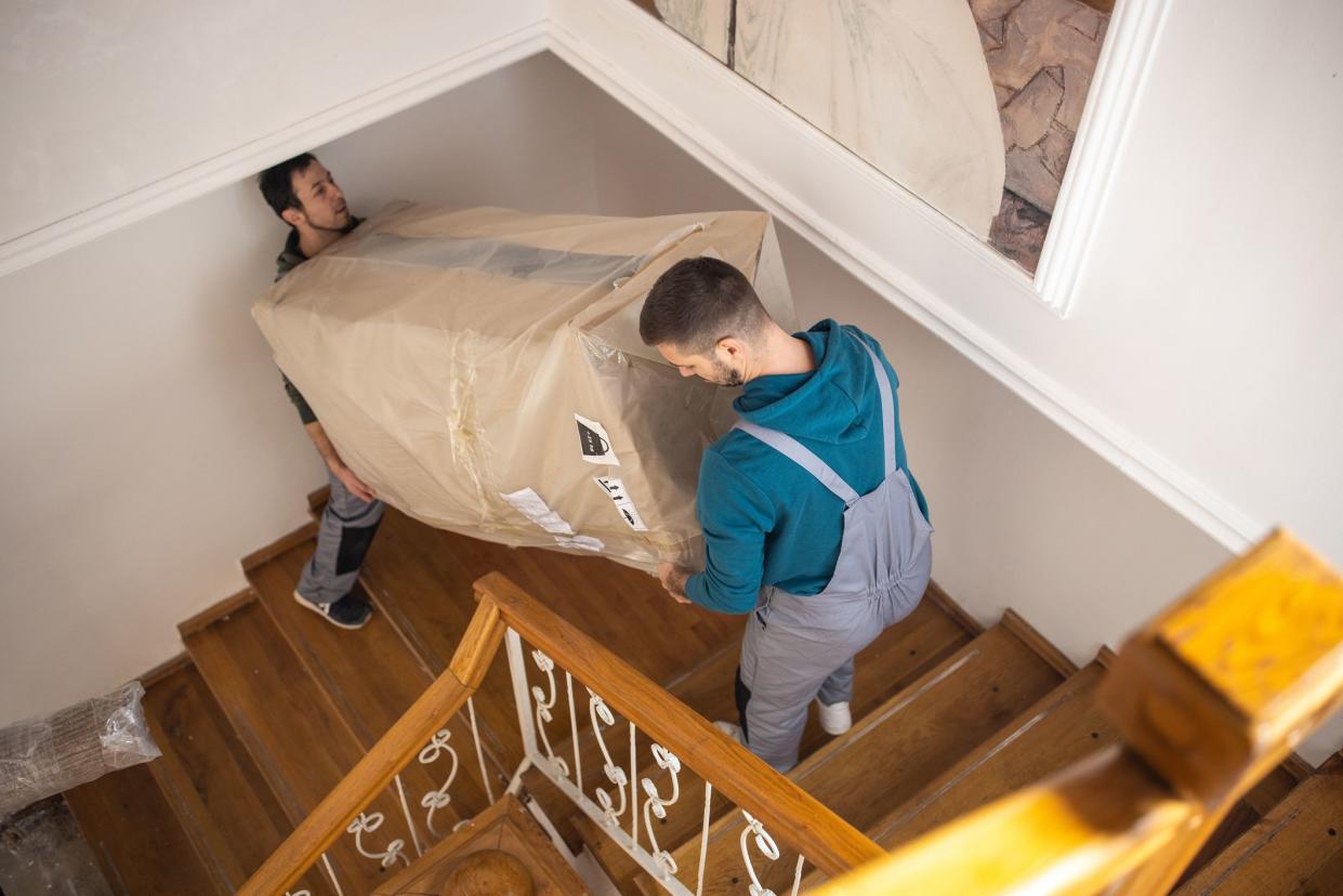 Professional movers moving up on staircase and carrying large box with furniture on first floor of house