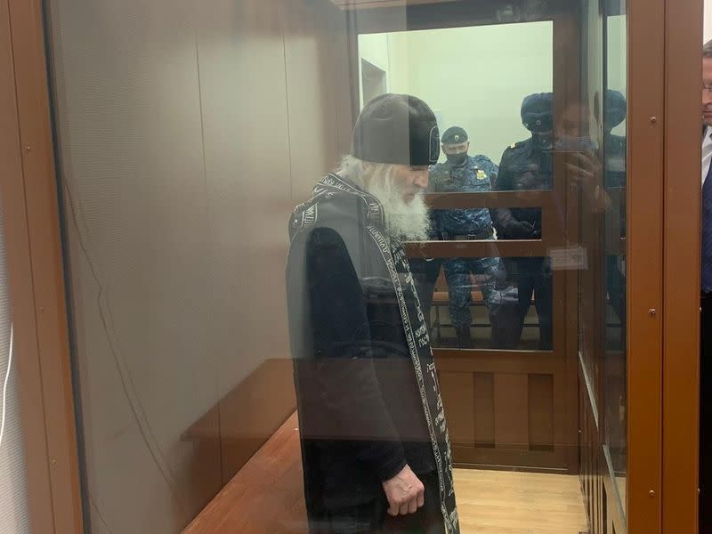 Father Sergiy Romanov, a coronavirus-denying priest suspended by the Russian Orthodox Church for disobeying orders, stands inside a defendants' cage during a court hearing in Moscow