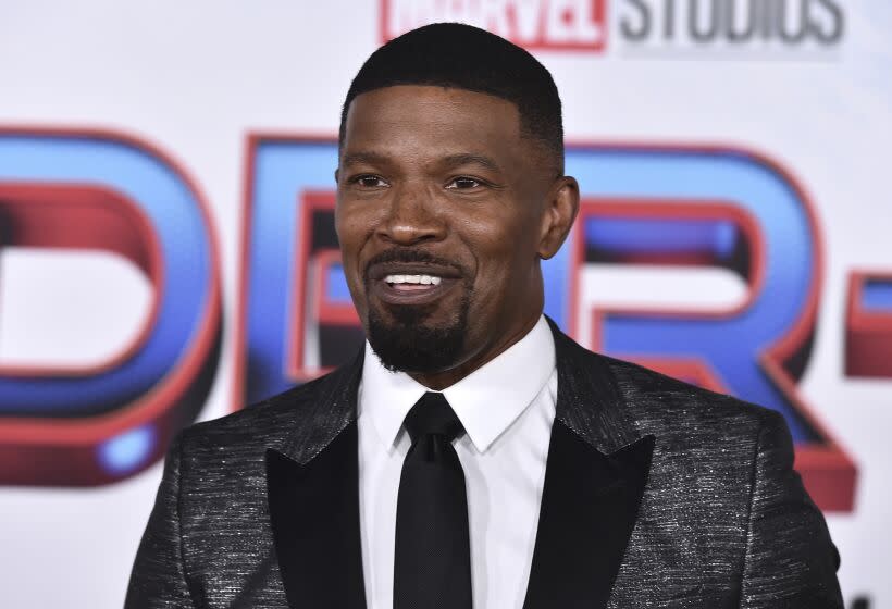 Jamie Foxx in a dark patterned suit and tie smiling for a a Spider-Man red carpet
