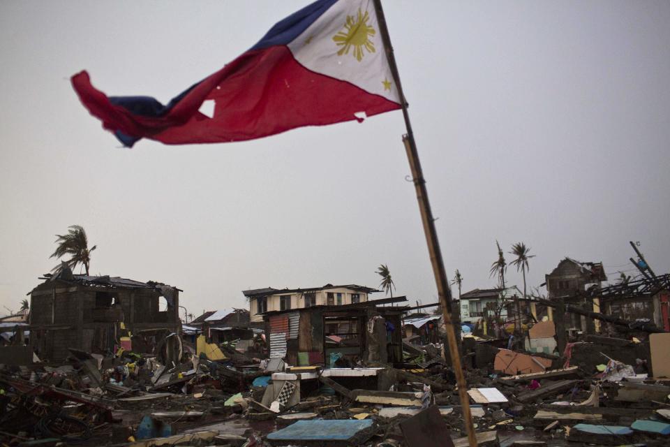 FILE - In this Friday Nov. 22, 2013 file photo, a flag of the Philippines flies over a destroyed neighborhood in Tacloban, Philippines. U.S. author Mitch Albom has launched a drive to rebuild 10 libraries in Tacloban, a central Philippine city ravaged by Typhoon Haiyan in November. National Book Store Foundation, his Philippine partner in the project, said Tuesday that Albom has pledged to raise $160,000, starting with his own contribution of $10,000 for the libraries. (AP Photo/David Guttenfelder, File)