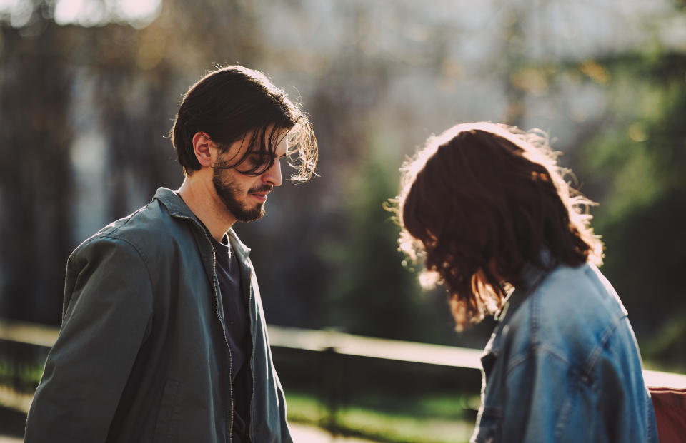 Serious boyfriend and his unrecognizable girlfriend looking down while standing together at the city street.