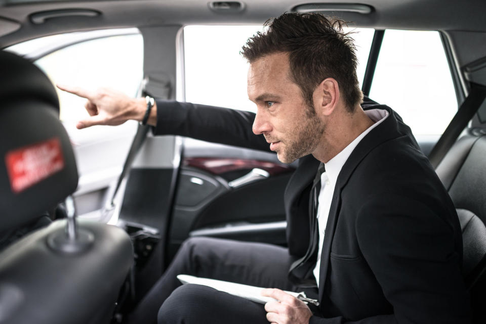 a man pointing from the back seat of a car