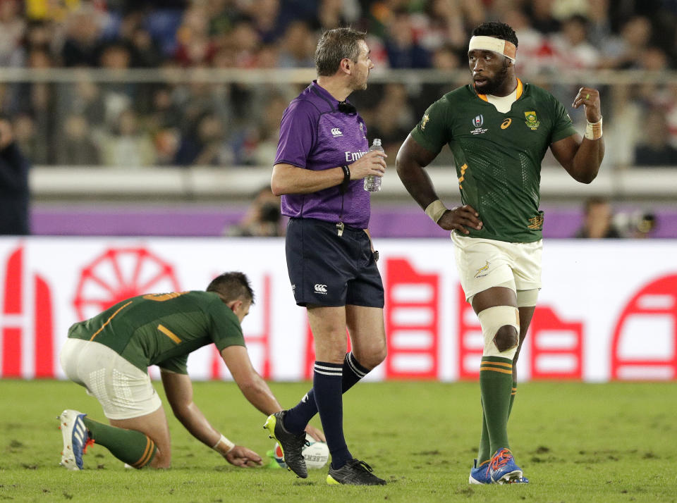South Africa's Siya Kolisi, right, talks with Referee Jerome Garces, as South Africa's Handre Pollard prepares for a penalty kick during the Rugby World Cup semifinal at International Yokohama Stadium between Wales and South Africa in Yokohama, Japan, Sunday, Oct. 27, 2019. (AP Photo/Aaron Favila)