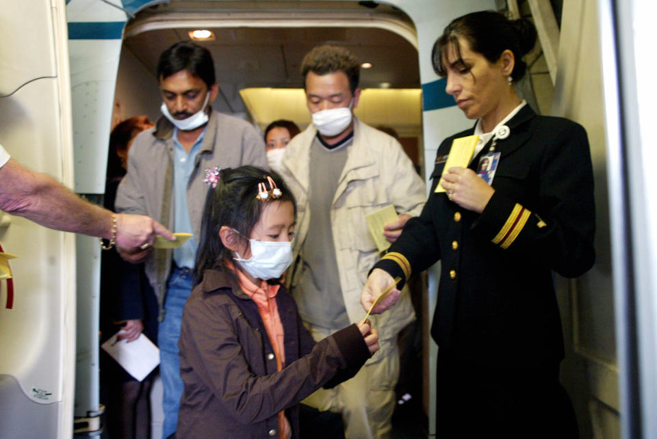 Pasajeros con cubrebocas que llegaron a Los Ángeles desde Hong Kong en 2003 durante el brote de SRAG reciben folletos que les aconsejan monitorear su salud durante 10 días. (Monica Almeida/The New York Times)