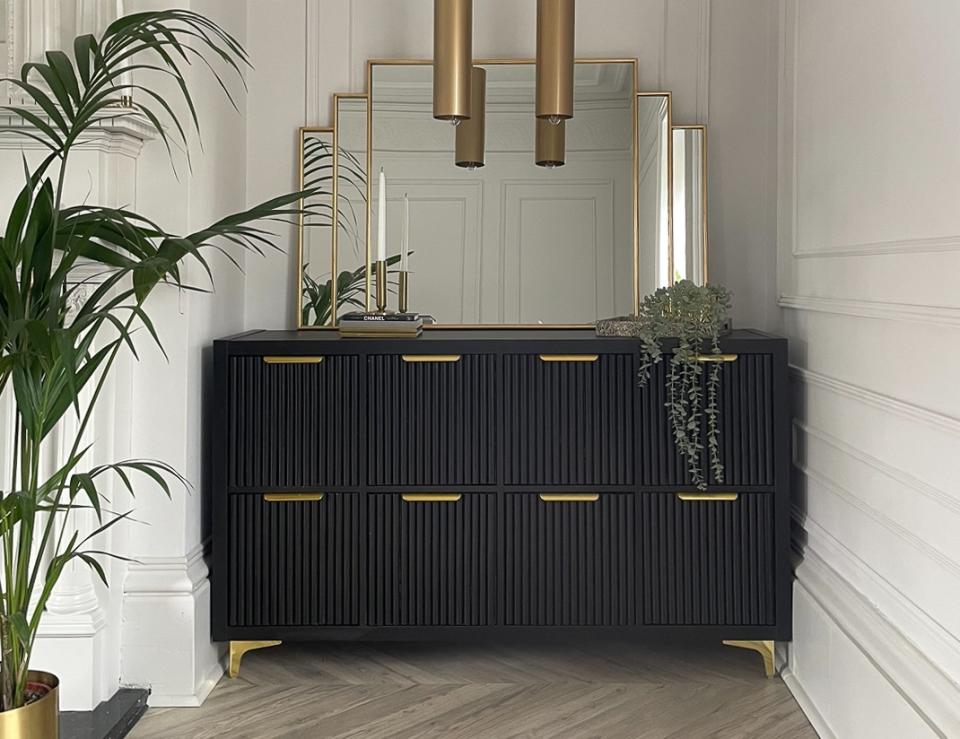 A fluted art deco style credenza in a nook with gold hardware and a gold framed mirror above it