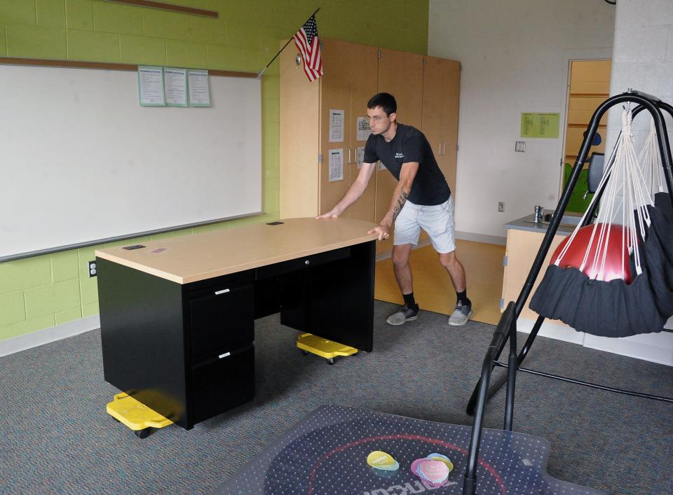 Green Local District head custodian Connor Madding pushes a teacher's desk back into a classroom.