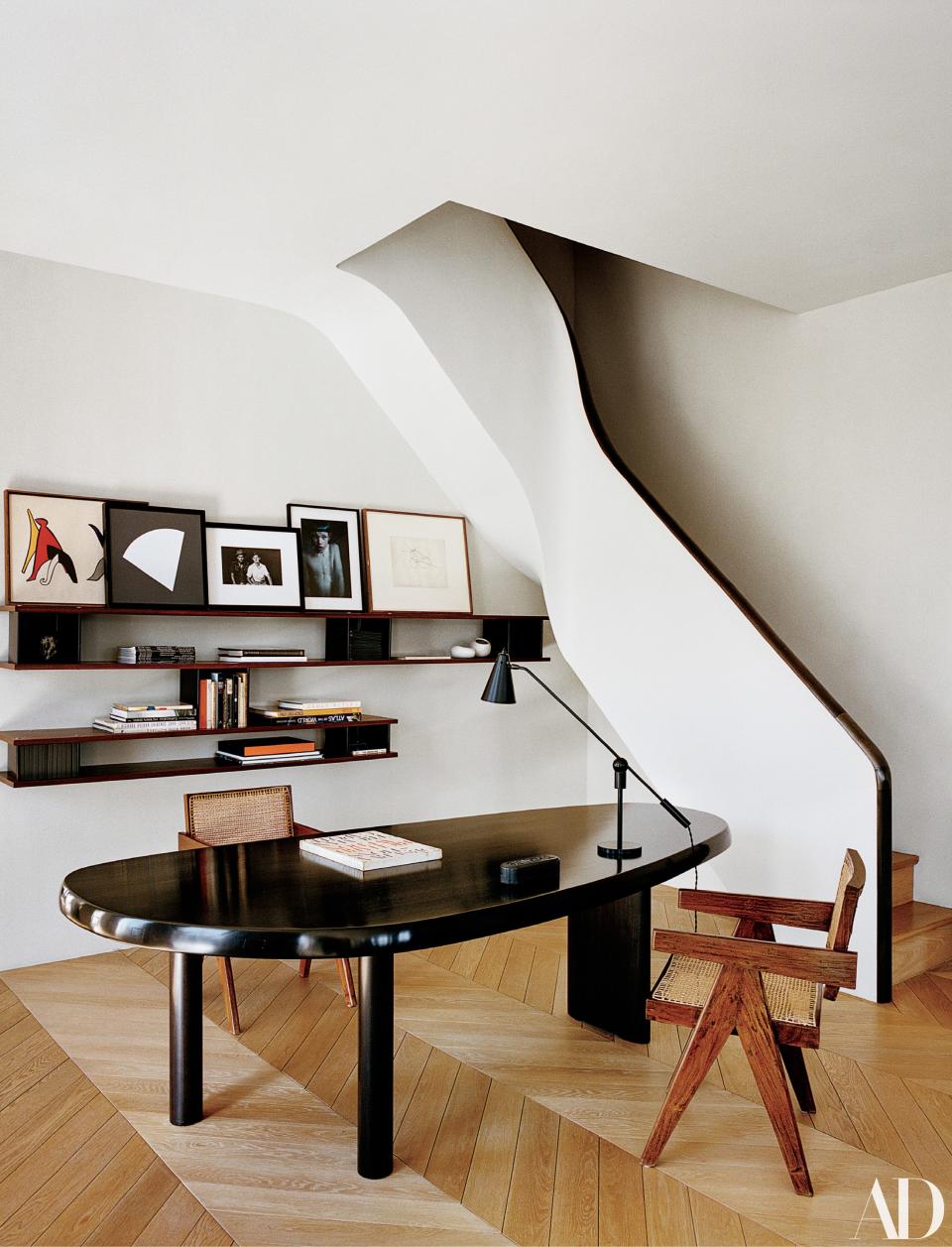 A stair twists into the living room. Charlotte Perriand table and bookshelf; Pierre Jeanneret armchairs; desk lamp from <a rel="nofollow noopener" href="https://wyeth.nyc/" target="_blank" data-ylk="slk:Wyeth;elm:context_link;itc:0;sec:content-canvas" class="link ">Wyeth</a>.