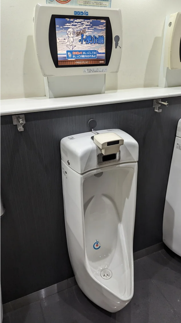 A video game screen mounted above a urinal in a restroom