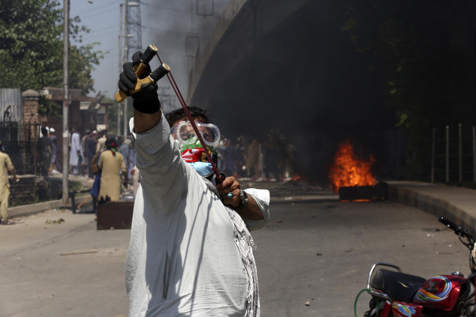 A supporter of Pakistan's former Prime Minister Imran Khan throws stones using a slingshot toward police officers during a protest against the arrest of their leader in Peshawar, Pakistan, Wednesday, May 10, 2023. Pakistan braced for more turmoil a day after Khan was dragged from court in Islamabad and his supporters clashed with police across the country. The 71-year-old opposition leader is expected in court later Wednesday for a hearing on keeping Khan in custody. (AP Photo/Muhammad Sajjad)