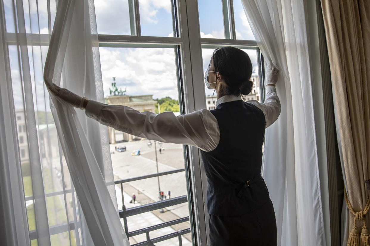 A hotel housekeeper opens curtains on a window facing the Brandenburg Gate in Berlin.