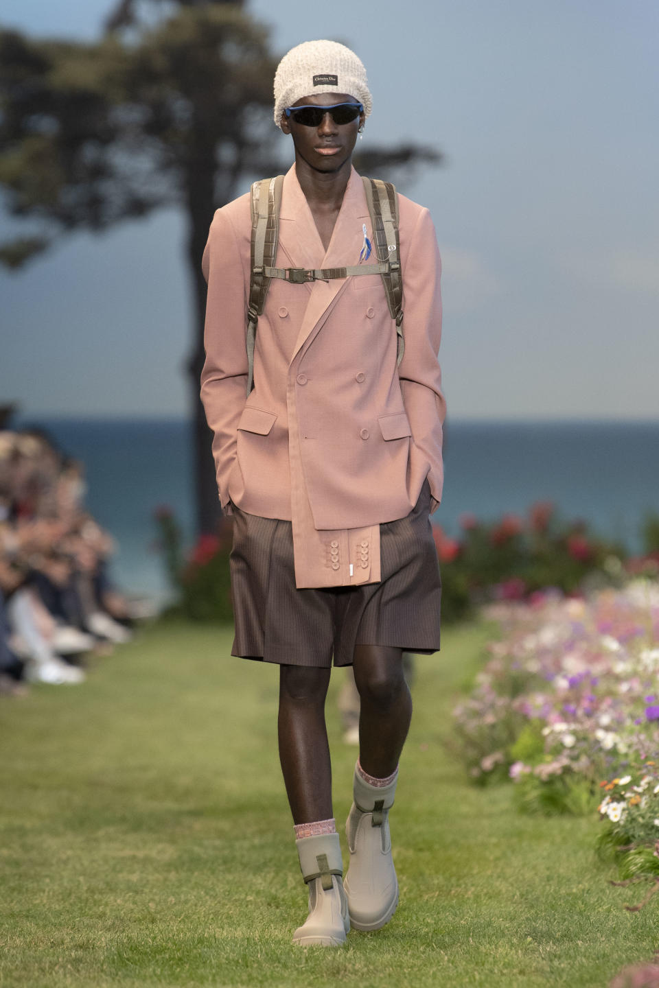 A double-breasted jacket paired with trouser shorts, rubberized sport boots and a hiking backpack at Dior summer ’23 men’s. - Credit: YANNIS VLAMOS