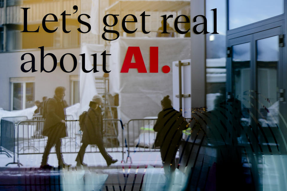 People reflected in a window of a hotel at the Davos Promenade with a slogan about AI alongside the World Economic Forum in Davos, Switzerland, Monday, Jan. 15, 2024. The AI technology has taken a large and growing slice of attention in Davos, this year the theme of Artificial Intelligence "as a driving force for the economy and society" will get about 30 separate sessions. (AP Photo/Markus Schreiber)