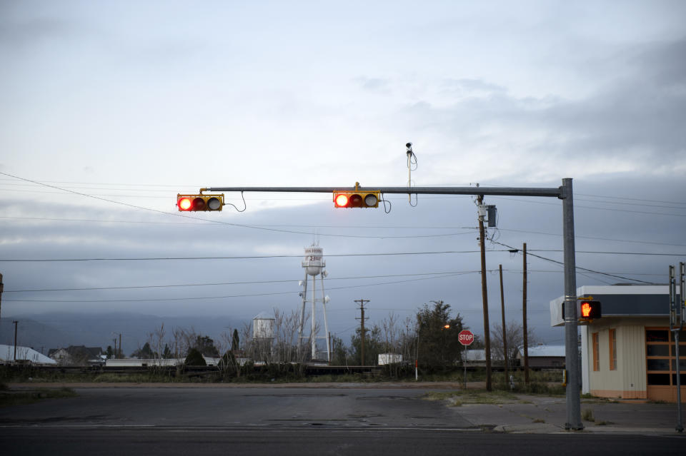 A deserted street intersection in a small town, showcasing traffic lights on red with an overcast sky in the background