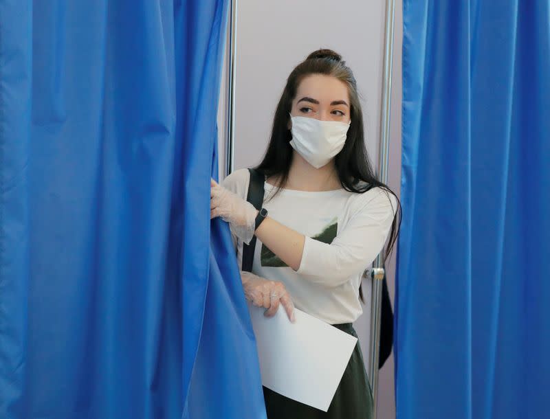 Woman wearing a protective face mask and gloves leaves a voting booth at a polling station during a seven-day nationwide vote on constitutional reforms in Russian embassy in Minsk