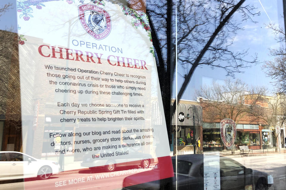 In this May 2, 2020 photo, a nearly deserted Front Street is reflected in the window of Cherry Republic, a popular downtown store that sells products made with the region's signature fruit in Traverse City, Mich. It's one of many local tourist-oriented businesses that have shut down during the coronavirus pandemic. With summer vacation season looming, this town on a Lake Michigan bay normally would be expecting a crush of visitors. But festivals are canceled and shops shuttered across the region, and some local residents have mixed feelings about crowds descending on the area, which might cause the number of virus cases to rise. (AP Photo/John Flesher)