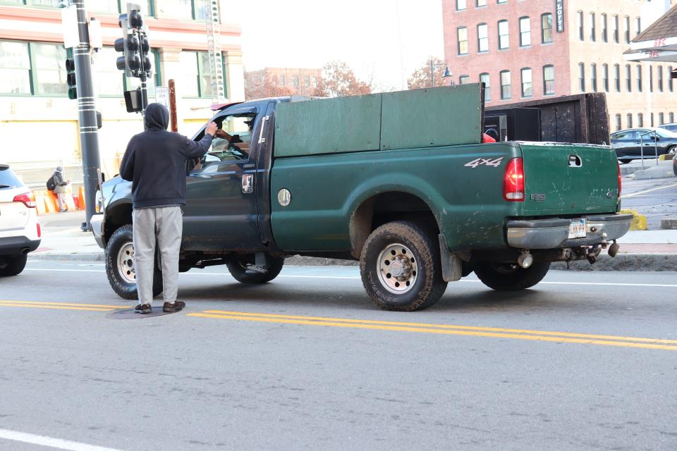 The driver of a truck rolls down their window and hands something to the man on Centre Street in downtown Brockton.