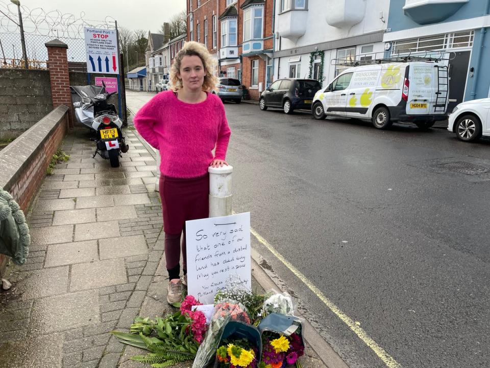 Heather, from the Portland Global Friendship Group, next to flowers laid in memory of the man who died on the Bibby Stockholm vessel (The Independent)
