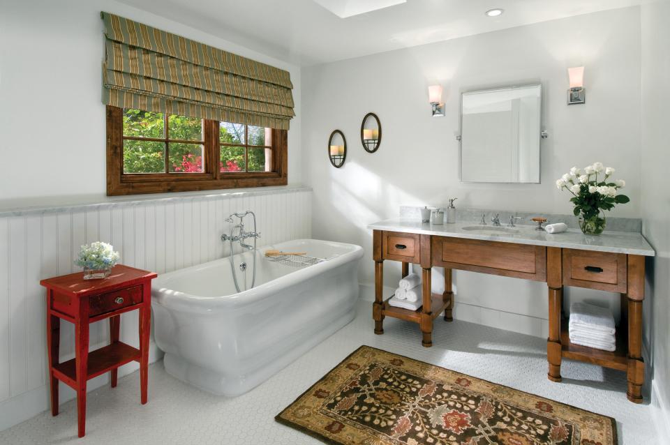 A white bathroom with a tub on the left and a wooden vanity with a marble countertop and sink on the right