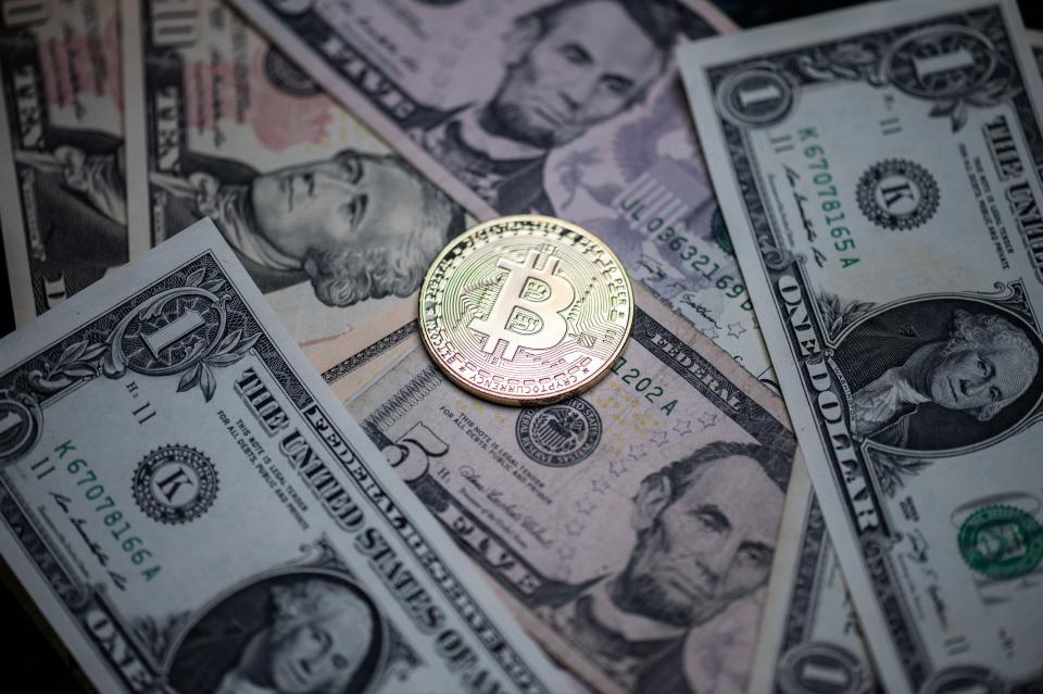 Photograph taken in Paris shows a physical imitation of the Bitcoin crypto currency displayed on US dollars bank notes (AFP via Getty Images)