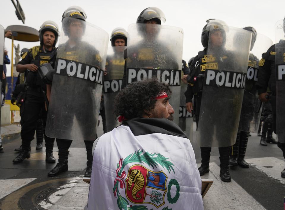 Un hombre se sienta en la calle frente a una línea de policías con equipos antidisturbios durante una marcha contra la presidenta peruana Dina Boluarte en Lima, Perú, el martes 17 de enero de 2023. (AP Foto/Martín Mejía)