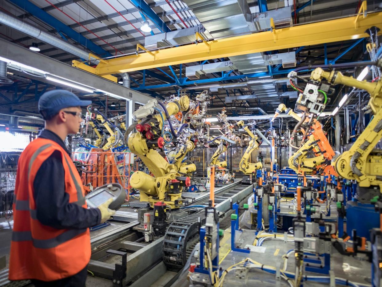 An apprentice engineer programming robots in a car factory.