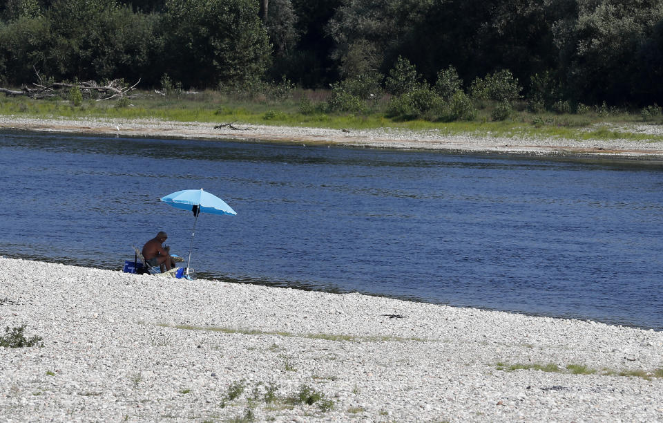 A man relaxes next to Ticino river in Bereguardo, near Pavia, Italy, Friday, Aug. 3, 2018. Hot air from Africa is bringing a heat wave to Europe, prompting health warnings about Sahara Desert dust and exceptionally high temperatures that could peak at 47 degrees Celsius (117 Fahrenheit). (AP Photo/Antonio Calanni)