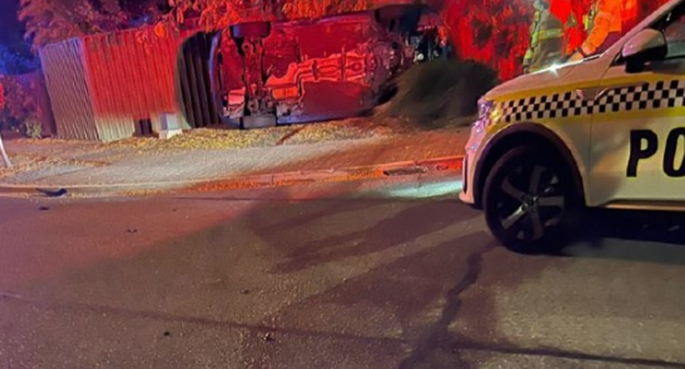 Police car with it's siren illuminating the couple's crashed car on it's side with red light. 