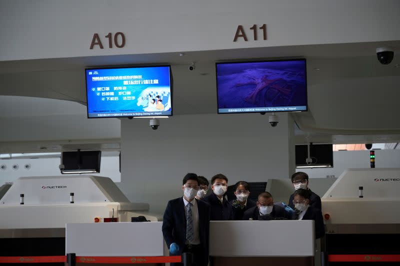 Staff members wearing face masks and glasses are seen at a counter at the Beijing Daxing International Airport