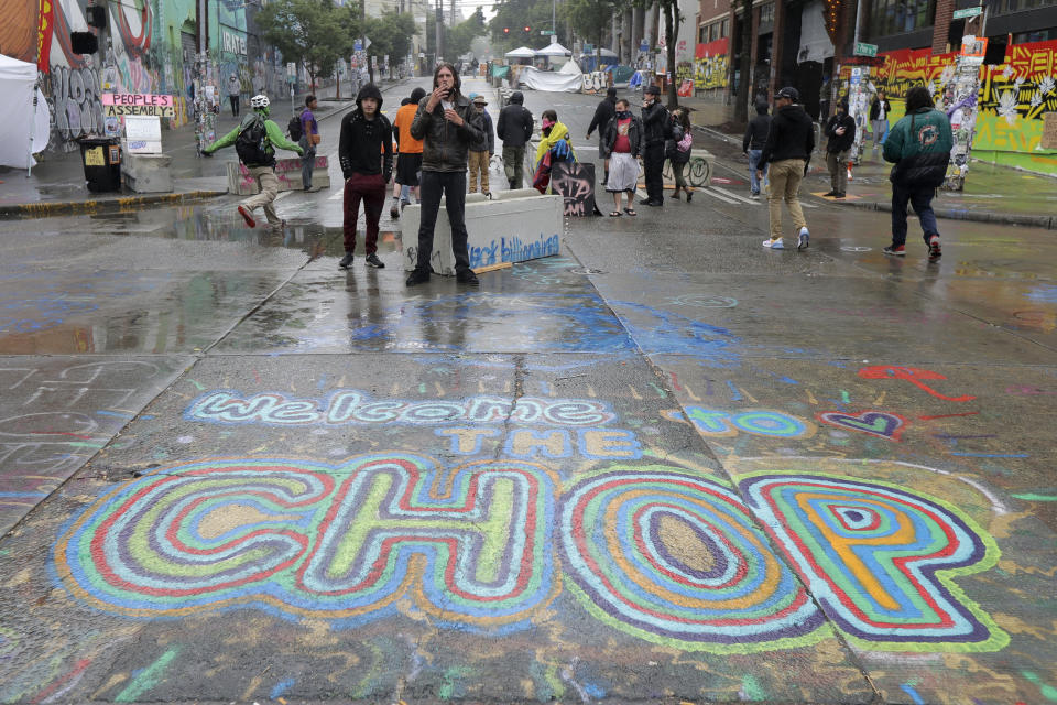 A sign on the street reads "Welcome to the CHOP" as protesters stand near barricades, Tuesday, June 30, 2020 at the CHOP (Capitol Hill Occupied Protest) zone in Seattle. Seattle Department of Transportation workers removed barricades about a block away Tuesday at the intersection of 10th Ave. and Pine St., but protesters quickly moved couches, trash cans and other materials in to replace the cleared barricades. The area has been occupied by protesters since Seattle Police pulled back from their East Precinct building following violent clashes with demonstrators earlier in the month. (AP Photo/Ted S. Warren)