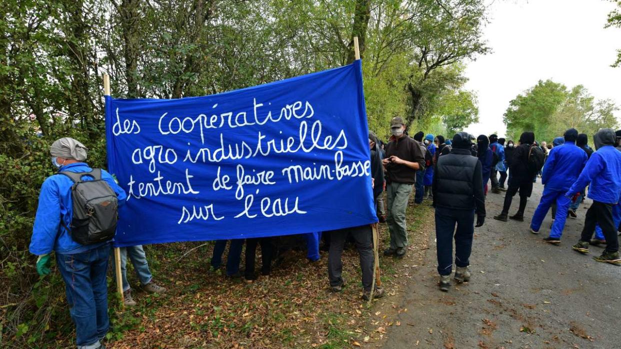 Des manifestants tiennent une banderole sur laquelle on peut lire « Les coopératives agro-industrielles tentent de se servir en eau » lors d’une manifestation contre un projet de bassin de rétention d’eau géant, près du site de construction d’une nouvelle réserve d’eau pour l’irrigation agricole, à Sainte-Soline, dans l’ouest de la France, le 30 octobre 2022. - Les protestations se sont poursuivies le 30 octobre, un jour après que des milliers de manifestants ont bravé une interdiction officielle pour défiler contre le déploiement d’une nouvelle infrastructure de stockage d’eau pour l’irrigation agricole dans l’ouest de la France, certains se heurtant à la police. Le groupe de pression « Bassines Non Merci », qui a organisé la manifestation, rassemble des associations environnementales, des syndicats et des groupes anticapitalistes contre ce qu’il considère comme un « accaparement de l’eau » par l’« agro-industrie » dans l’ouest de la France. (Photo : pascal lachenaud / AFP)