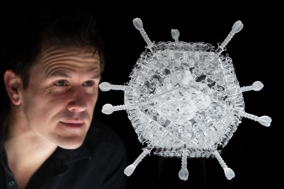 EMBARGOED TO 1200 FRIDAY FEBRUARY 5 Bristol-based artist Luke Jerram looks at his glass sculpture of the Oxford-AstraZeneca vaccine, made to mark the ten millionth vaccination in the UK. The artwork measures 34cm across and is one million times larger than the actual nanoparticle. It has been created using borosilicate glass and the same materials and techniques used in the manufacture of medical scientific glassware for test tubes and distilleries. Picture date: Friday February 5, 2021.