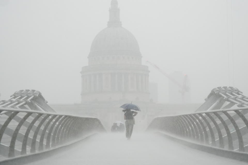 People with umbrellas walking in the rain on Millennium Bridge, London.