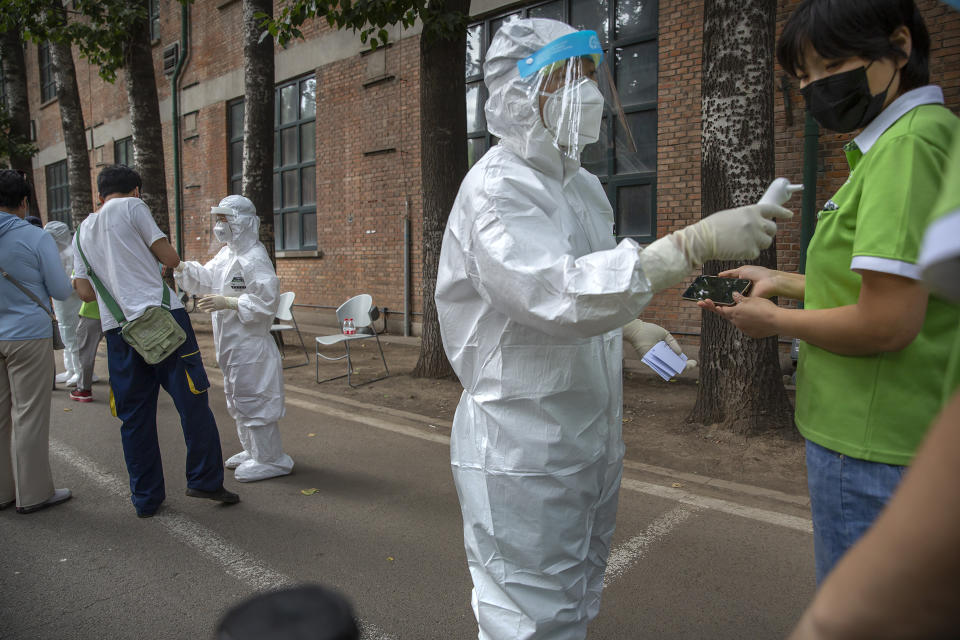 Workers in protective suits take the temperatures of people at a COVID-19 testing site for those who were potentially exposed to the coronavirus outbreak at a wholesale food market in Beijing, Wednesday, June 17, 2020. As the number of cases of COVID-19 in Beijing climbed in recent days following an outbreak linked to a wholesale food market, officials announced they had identified hundreds of thousands of people who needed to be tested for the coronavirus. (AP Photo/Mark Schiefelbein)