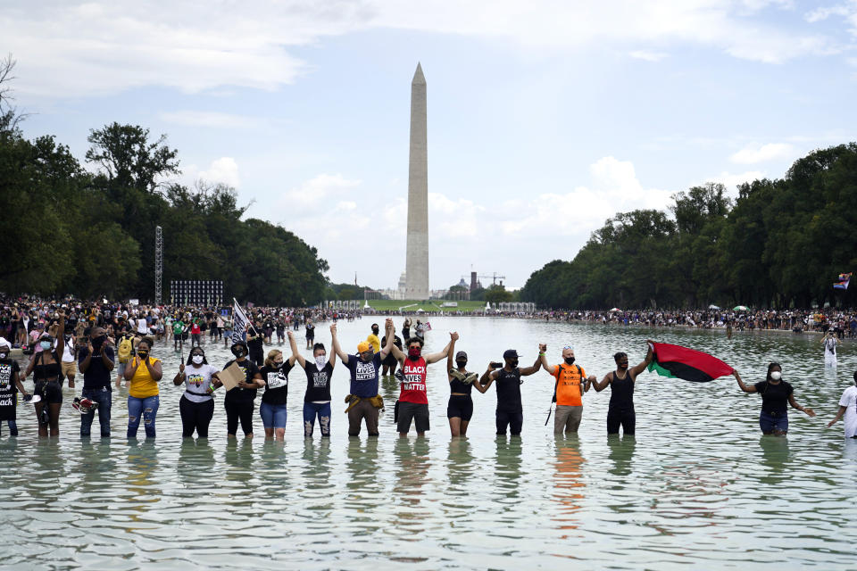 People pose for a photo in the Reflecting Pool in the shadow of the Washington Monument as they attend the March on Washington, Friday, Aug. 28, 2020, at the Lincoln Memorial in Washington, on the 57th anniversary of the Rev. Martin Luther King Jr.'s "I Have A Dream" speech. (AP Photo/Julio Cortez)