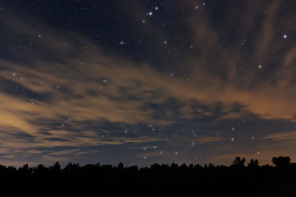 The night sky with bright white stars in the background covered by cream-colored clouds in the foreground.