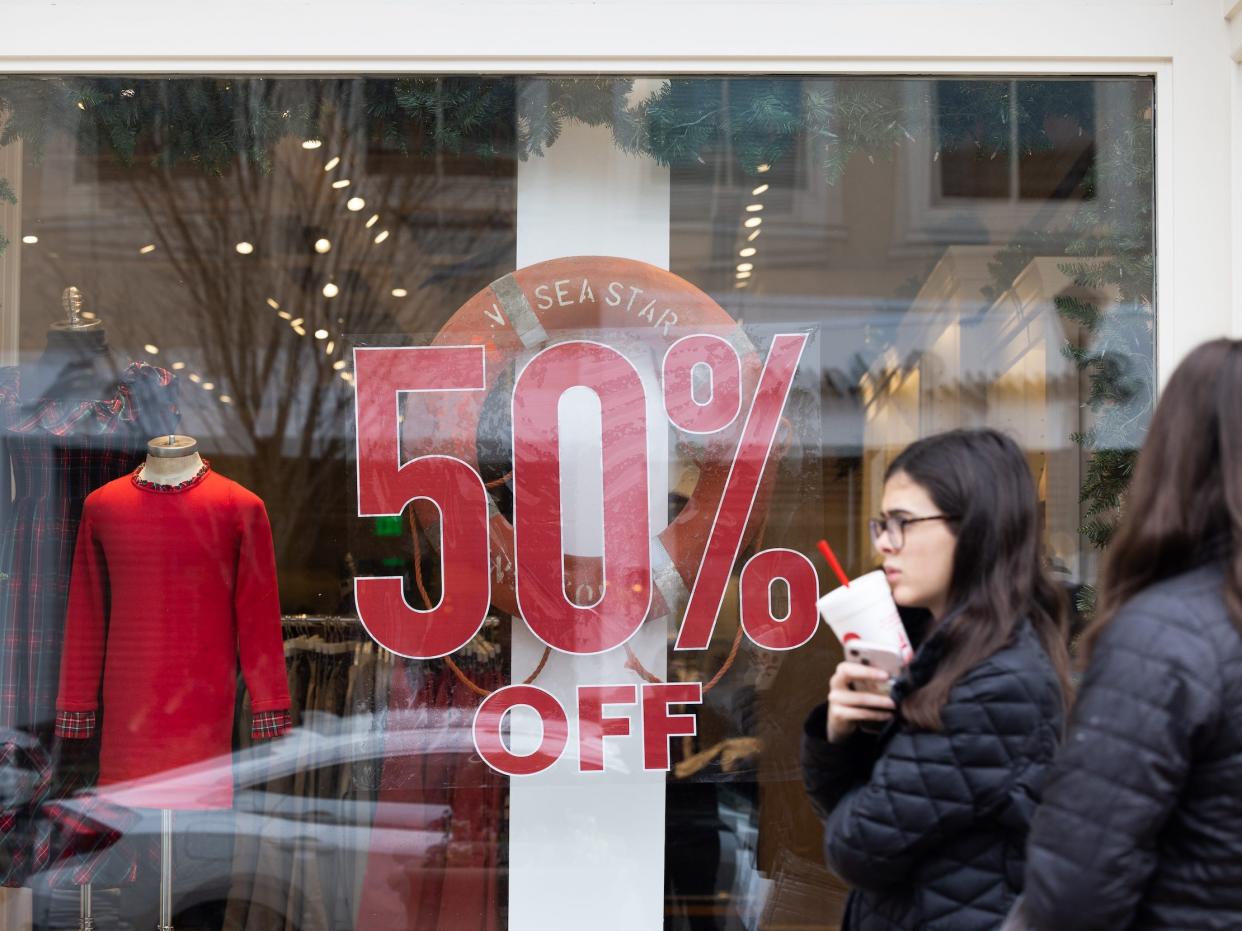 Woman walks past store window with sign reading "50% off"