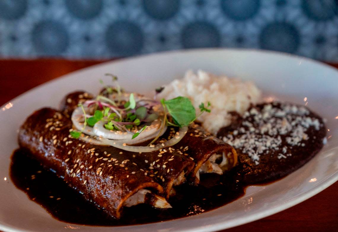 The enchiladas oaxaqueñas at Centro Is made with pulled chicken, mole negro, cream, cotija, and sesame seeds and served with steamed rice and refried black beans Thursday, Oct. 20, 2022.