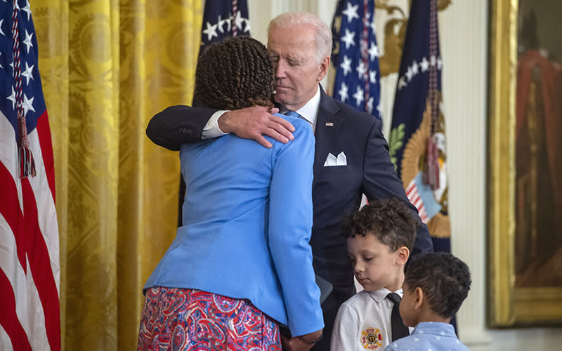 President Biden gives the Public Safety Officer Medal of Valor to Sabrail Davenport as he hugs her; there are two children in the foreground