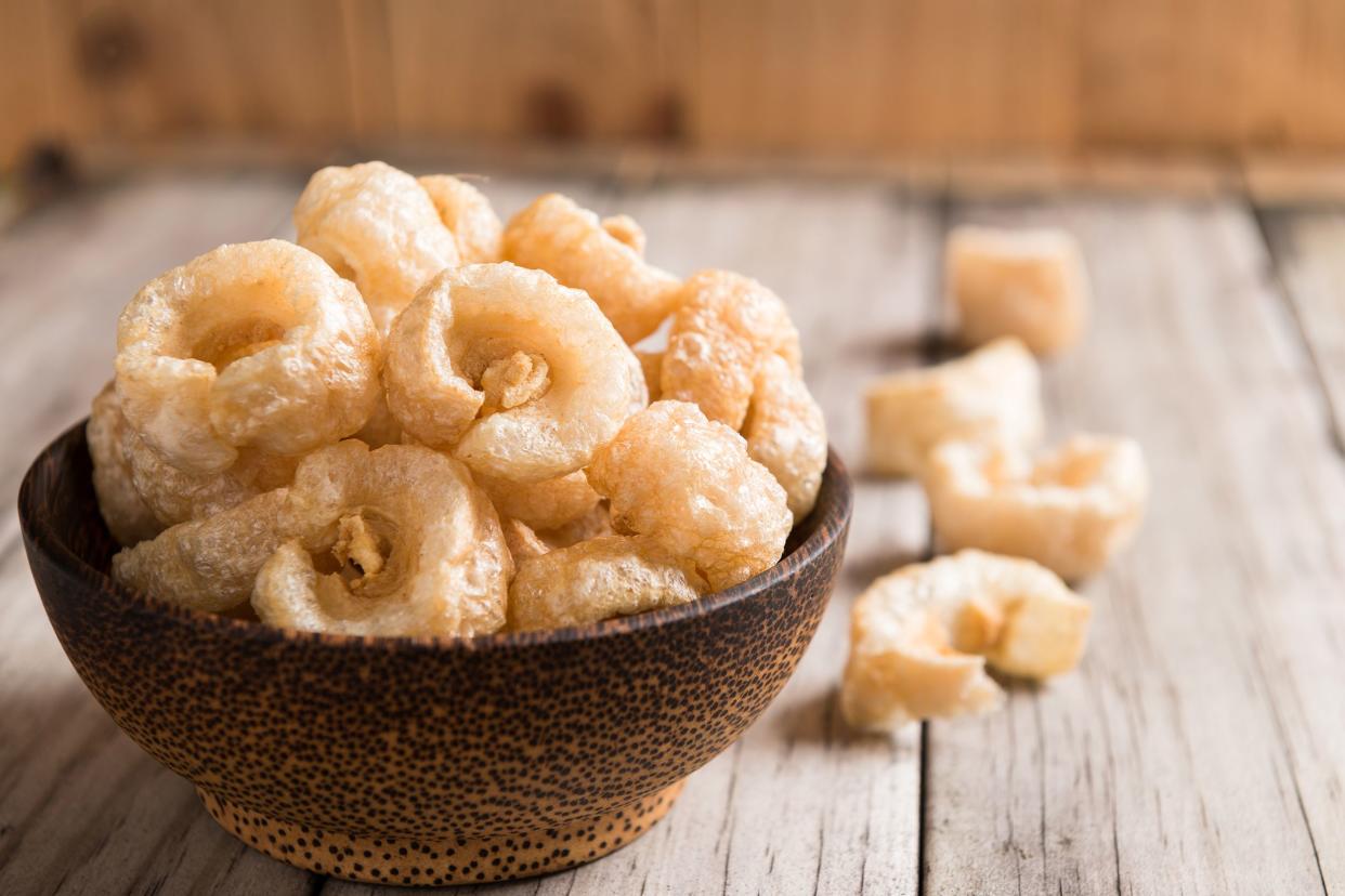 Closeup of ceramic bowl of pork rinds with a blurred background of a line of pork rines on a wooden table