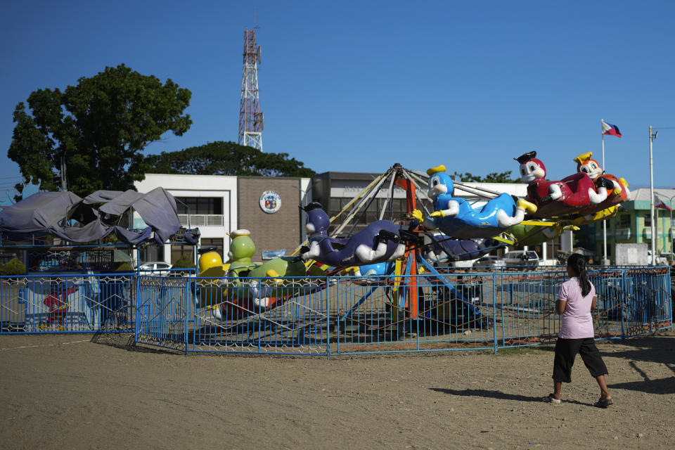 A woman walks past a carnival ride in front of the town municipal hall in Santa Ana, Cagayan province, northern Philippines, Tuesday, May 7, 2024. The United States and the Philippines, which are longtime treaty allies, have identified the far-flung coastal town of Santa Ana in the northeastern tip of the Philippine mainland as one of nine mostly rural areas where rotating batches of American forces could encamp indefinitely and store their weapons and equipment within local military bases under the Enhanced Defense Cooperation Agreement, or EDCA. (AP Photo/Aaron Favila)