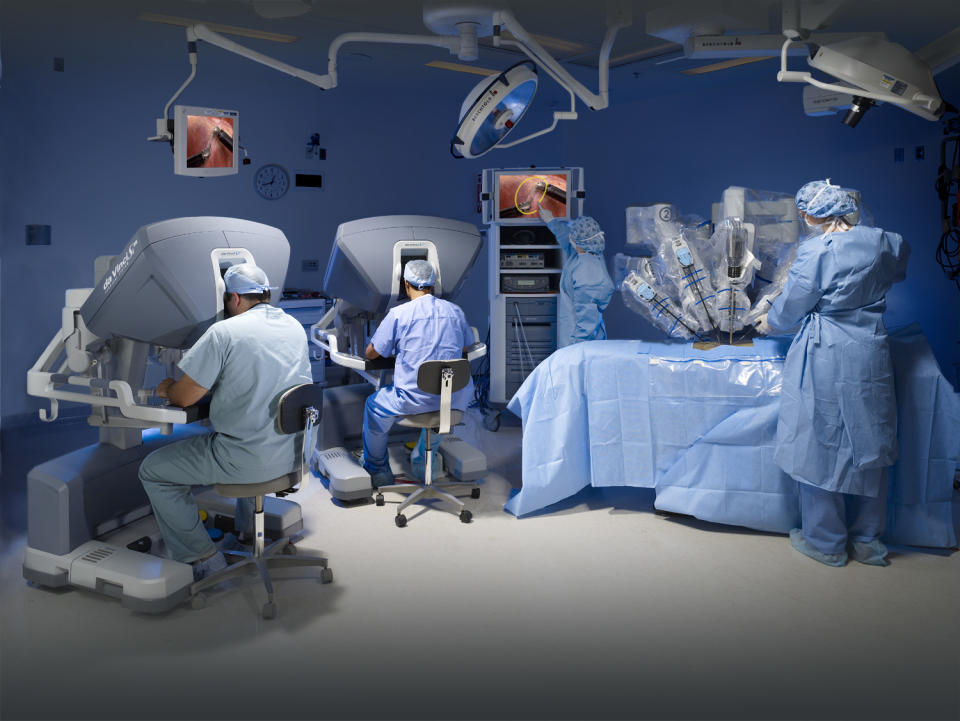 Two surgeons sitting at consoles in an operating room, with nurses in attendance conducting robotic surgery.