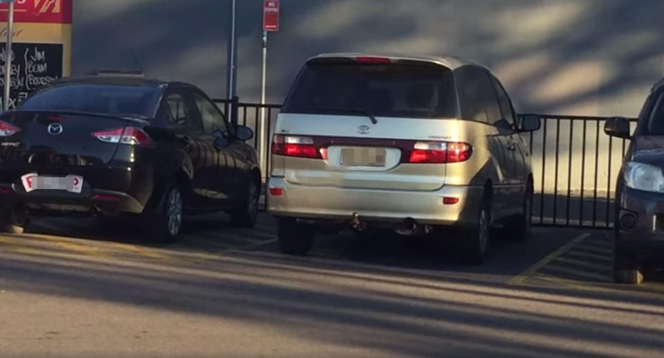 Two cars are seen parked either side of a van in a disabled spot at Liverpool in NSW. They're in the yellow zones blocking wheelchair access to either side of a van. 