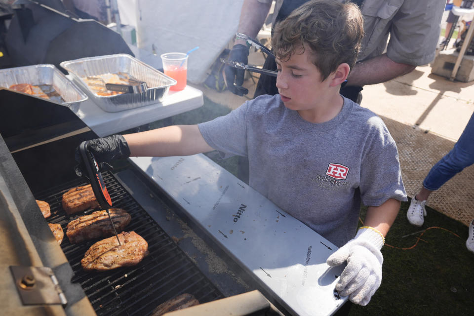 Miles O'Guin, 9, checks the temperature of pork chops on the grill at the World Championship Barbecue Cooking Contest, Friday, May 17, 2024, in Memphis, Tenn. (AP Photo/George Walker IV)