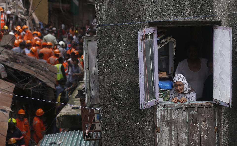 A woman looks from a window as rescuers work at the site of a building that collapsed in Mumbai, India, Tuesday, July 16, 2019. A four-story residential building collapsed Tuesday in a crowded neighborhood in Mumbai, India's financial and entertainment capital, and several people were feared trapped in the rubble, an official said. (AP Photo/Rafiq Maqbool)